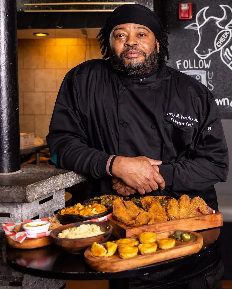Tracy M. Pressley Sr., Executive Chef at BUDA's Grille, presenting a spread of soul food including fried chicken, mac and cheese, cornbread, and collard greens